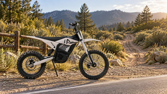 A white and black MUDLIZ electric dirt bike parked at the edge of an OHV trail beside a paved road
