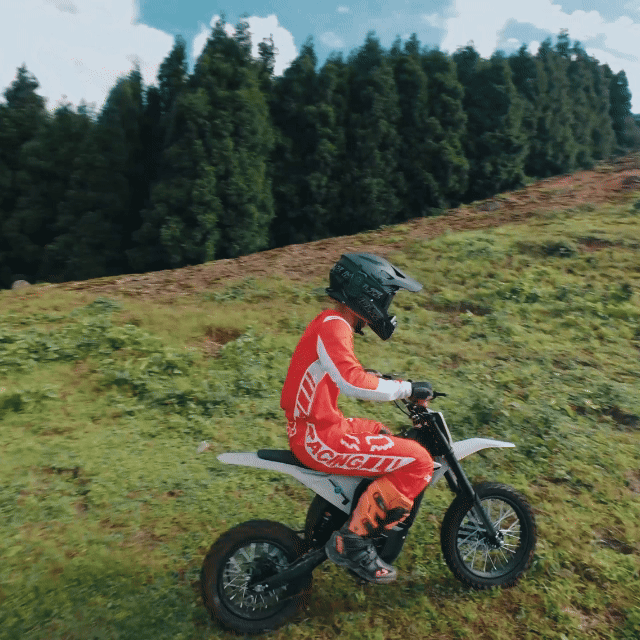 Rider in red crossing a grassy hillside on a Mudliz electric dirt bike