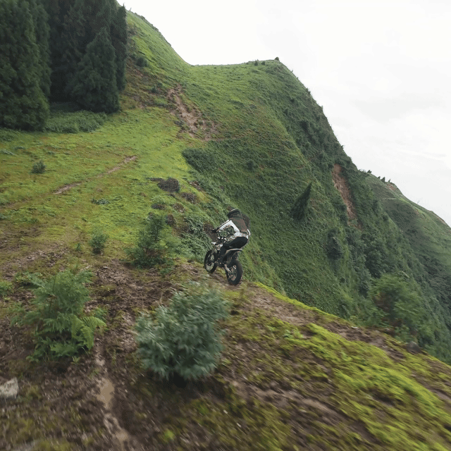 Rider descending a green hillside on an electric dirt bike