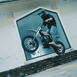 Rider jumping a Mudliz electric dirt bike near a building